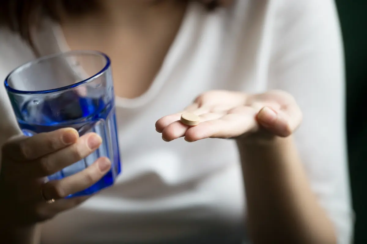 mujer con vaso tomando pastillas de megalevure