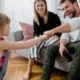 padre sentado sofa choca puño con hija y mujer detras