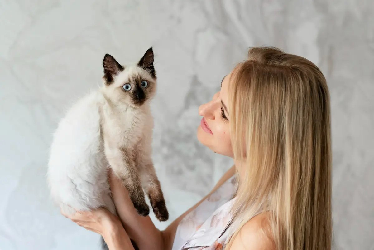 chica rubia sujeta su gata siamesa