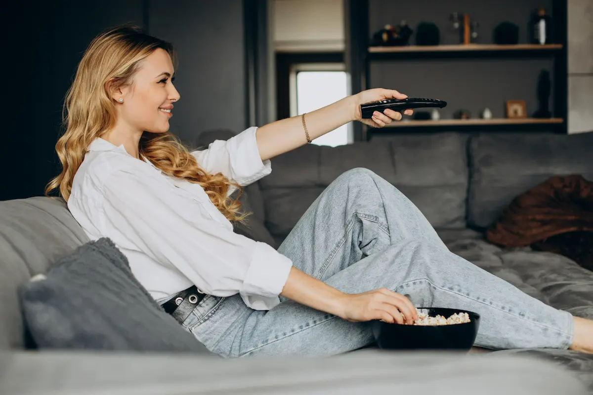 chica rubia tumbada con mando enciende la TV