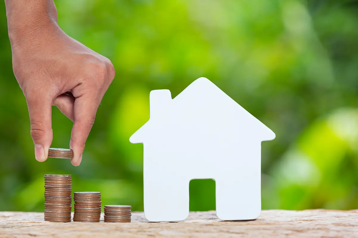 mano de hombre apila monedas a lado de casita