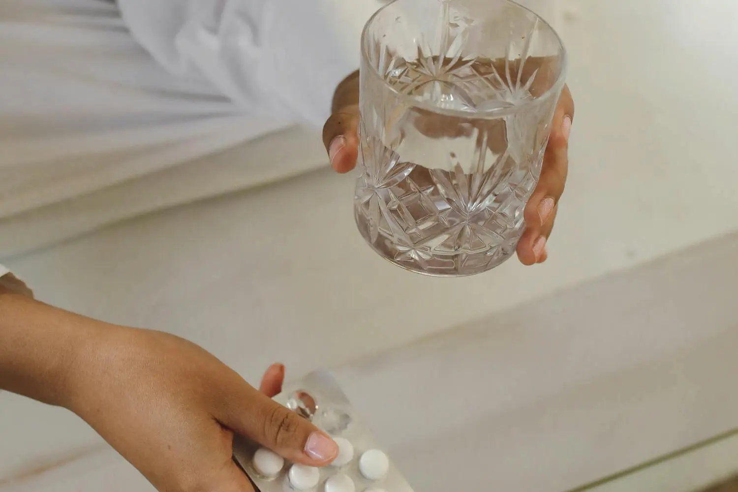 Blíster de comprimidos y vaso de agua sobre mesa, luz cálida