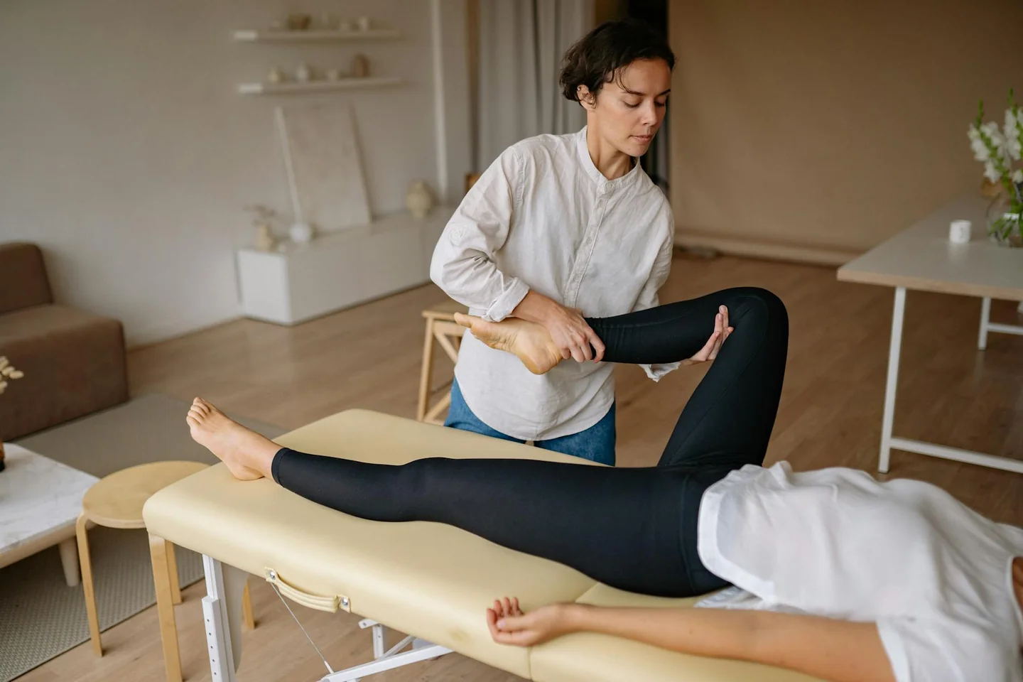 Mujer sentada en casa con gesto de dolor en las piernas, ilustrando porque tengo agujetas en las piernas sin hacer ejercicio