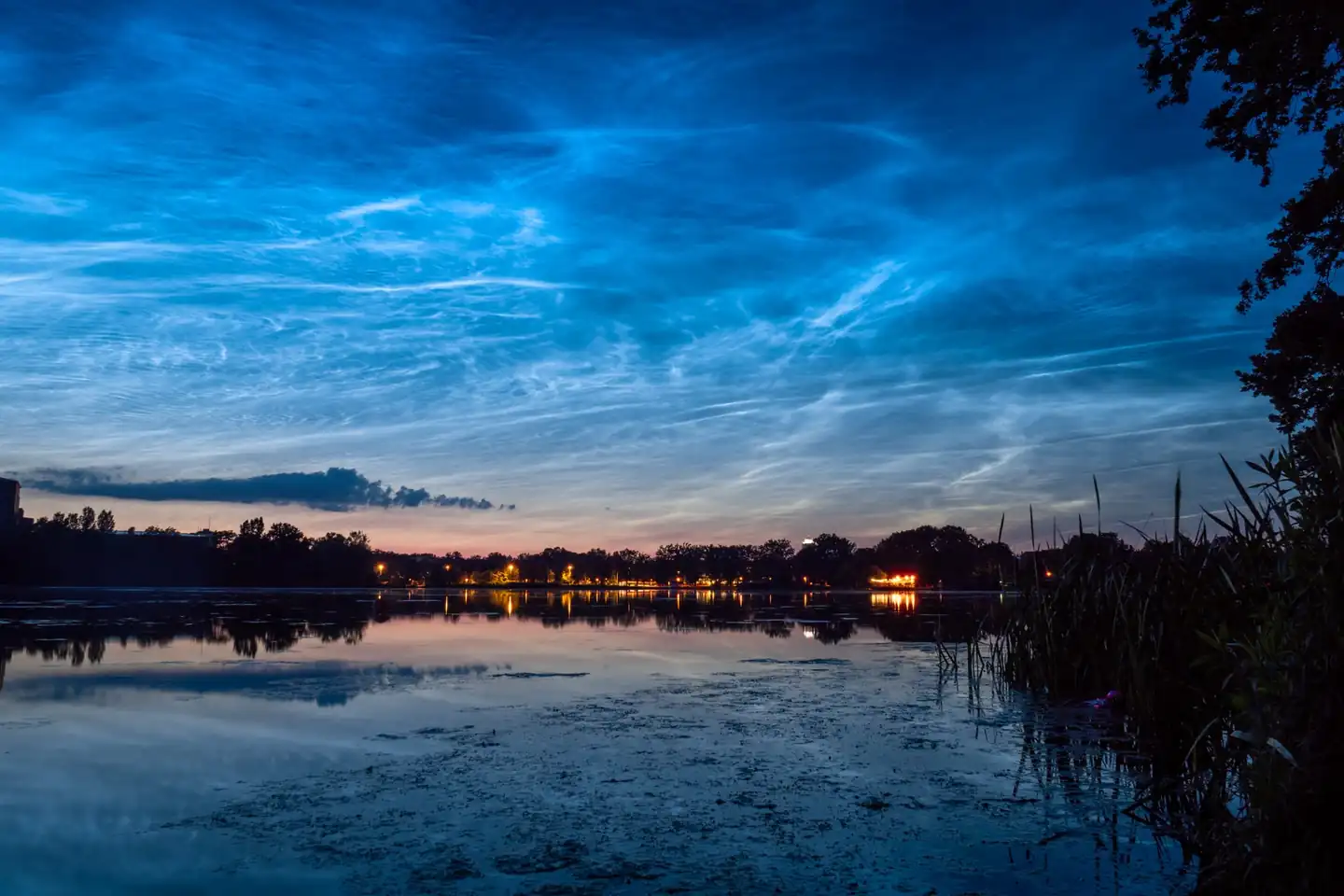 Imagen ilustrativa de qué son las nubes noctilucentes en un cielo crepuscular, con filamentos azulados brillando sobre el horizonte.