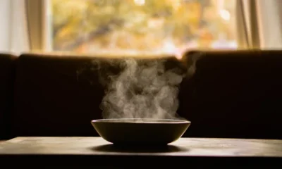 Persona que siente más hambre con frío y sostiene un plato de sopa caliente junto a una ventana