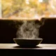 Persona que siente más hambre con frío y sostiene un plato de sopa caliente junto a una ventana