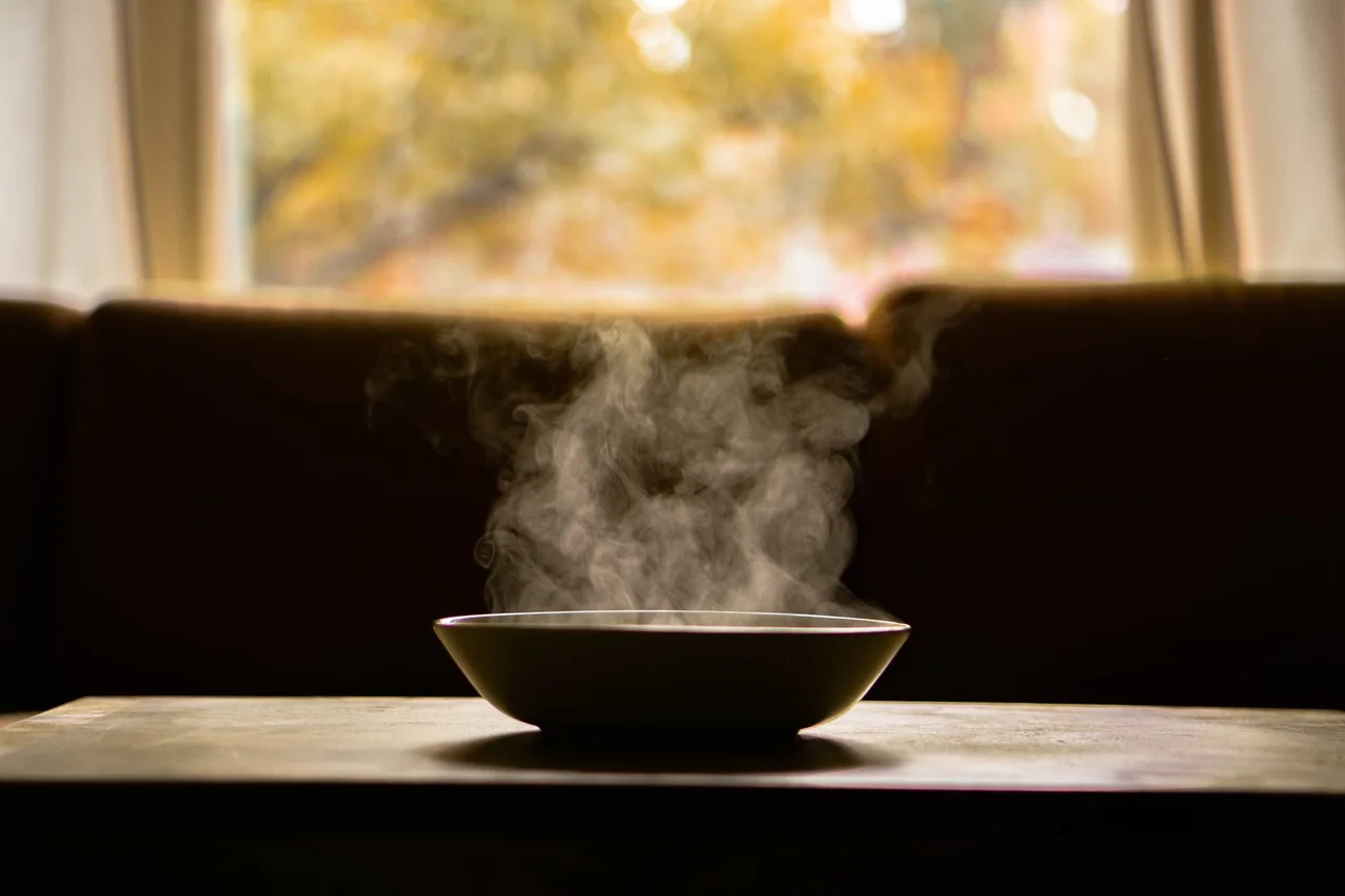 Persona que siente más hambre con frío y sostiene un plato de sopa caliente junto a una ventana