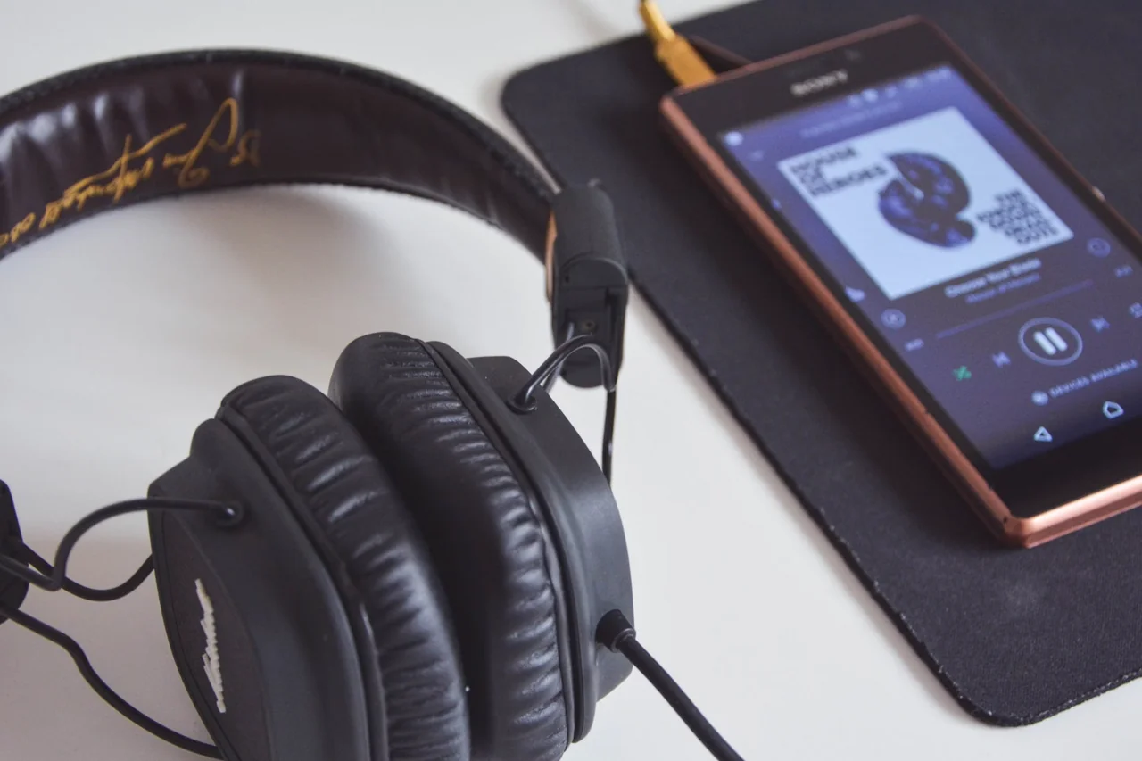 Teléfono con una aplicación de música abierta y auriculares, una escena que ilustra por qué algunas canciones dejan de aparecer en Spotify