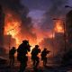 Soldados de fuerzas especiales avanzando al anochecer por una calle urbana en ruinas con explosiones al fondo