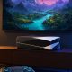 Consola de videojuegos futurista con mando iluminado junto a una television