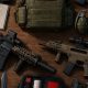 Equipo militar de mercenario sobre una mesa: rifles de asalto, blindaje, botiquín y cargadores